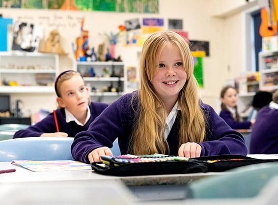 School girl with blonde hair sat at desk smiling