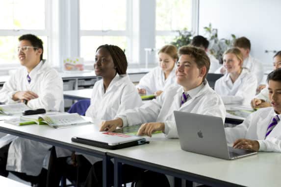 Senior school pupils sat at desks wearing lab jackets