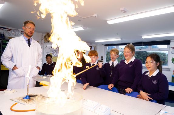 Prep school science teacher and pupils observing Chemistry experiment with flame.