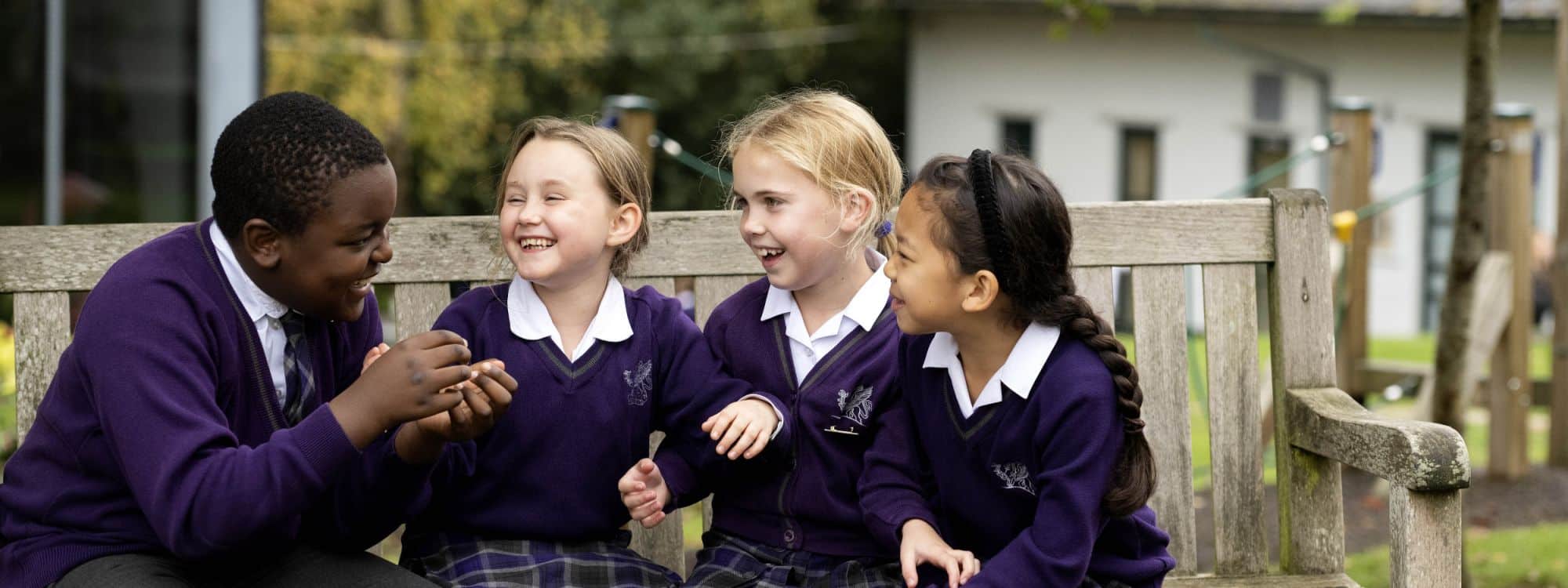 Group of school children laughing together, sat on bench