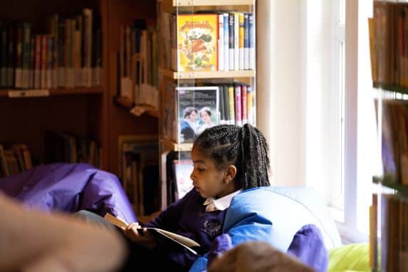 Independent boarding school girl in library sat on beanbag reading book