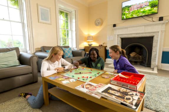 Three senior school girls in boarding house living room playing Monopoly