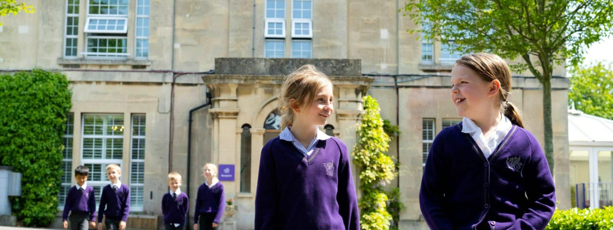 Two girls in foreground looking at each, four school pupils in background