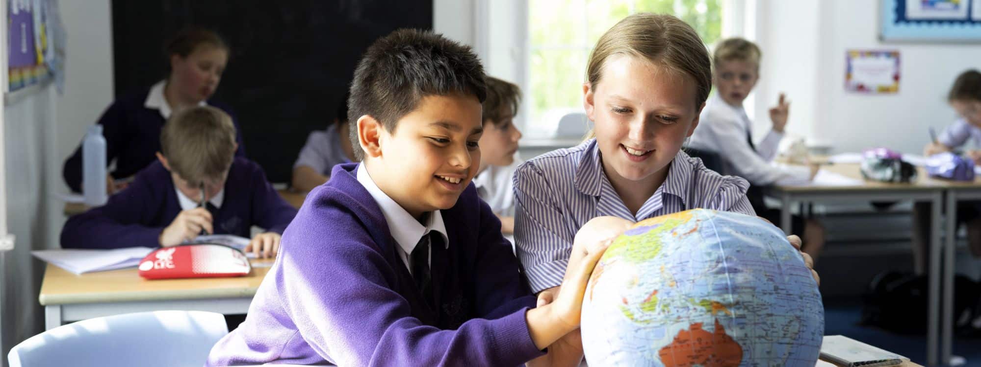 White prep girl and Asian prep boy observing world globe in classroom