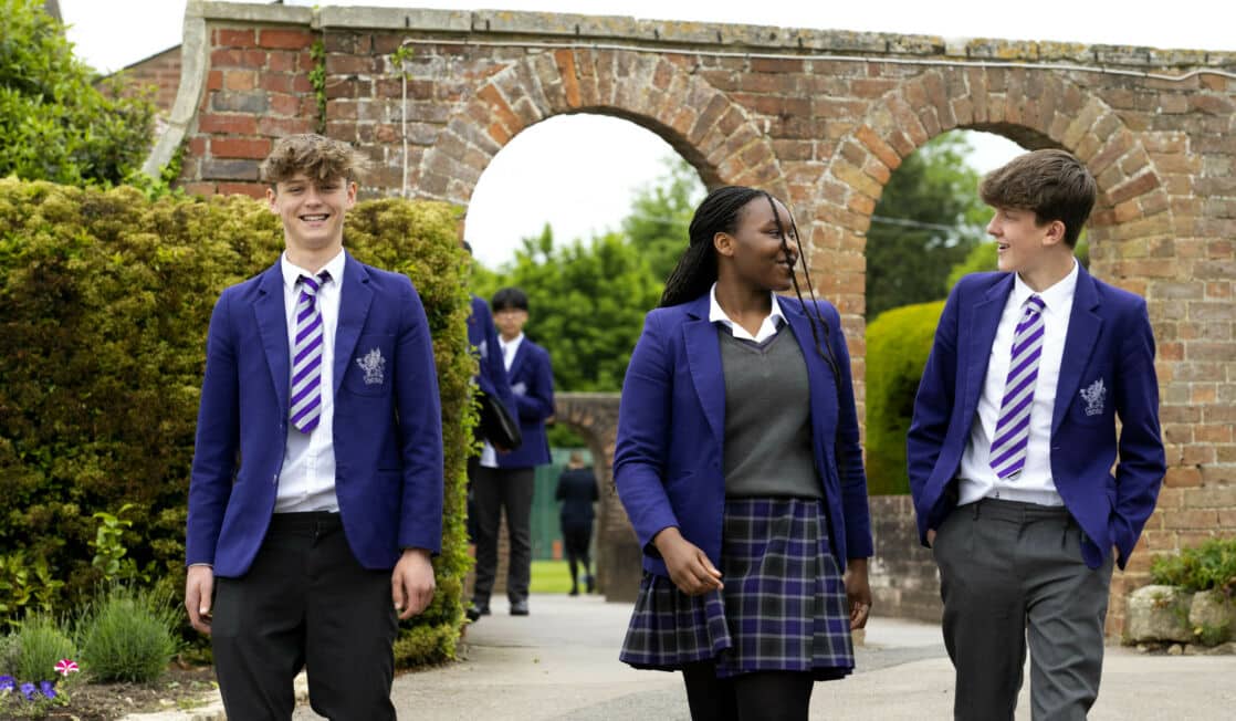 Two boy and one girl pupil walking together with characterful brick arches in background