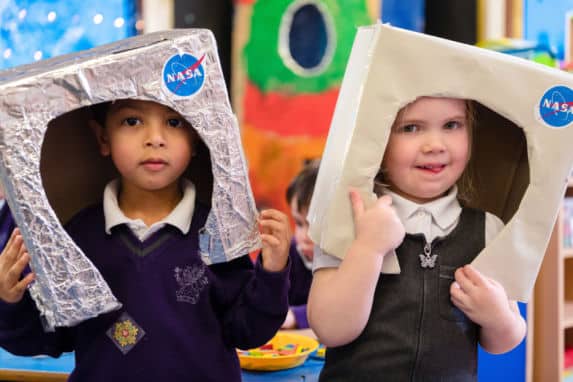 pre prep and nursery school children playing with crafted cardboard boxes on their heads