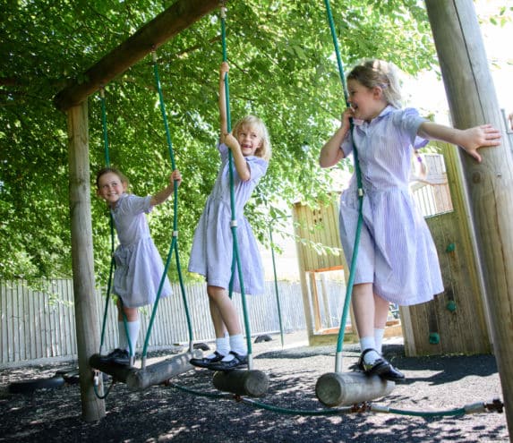 three pre prep girls in purple school dresses on outdoor play equipment