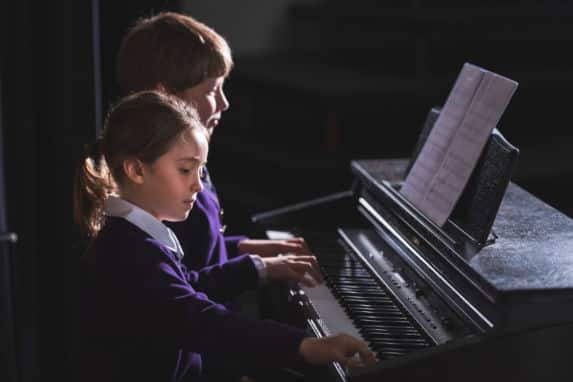 Prep school girl and boy playing piano together