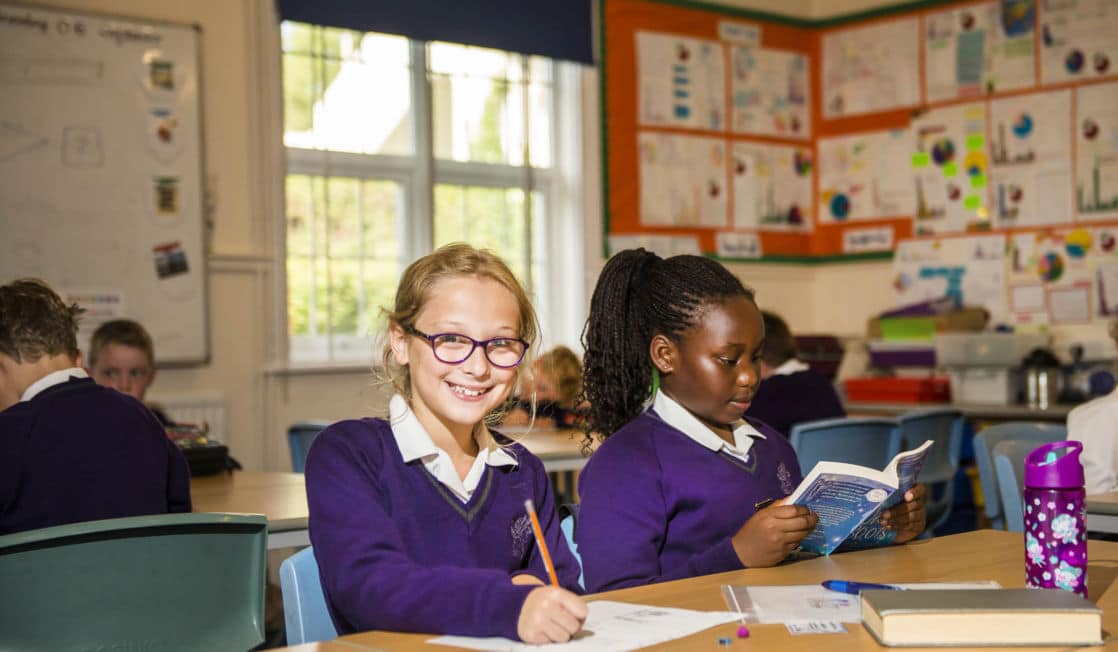 prep school girl sat at desk holding pencil, looking at camera