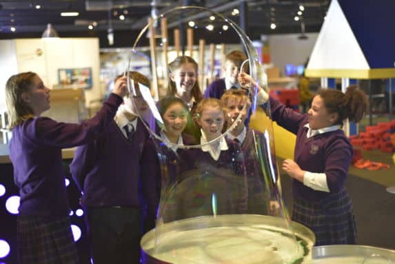 Group of school children at science centre playing with giant bubble hoop