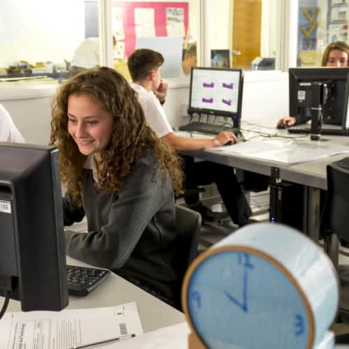 Smiling school girl with curly hair studying at computer